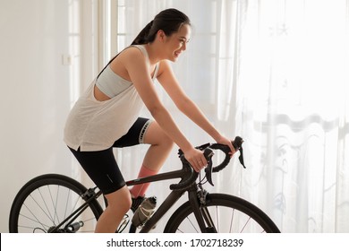 Asian Woman Cyclist. She Is Exercising In Home. She Cycling On The Trainer 