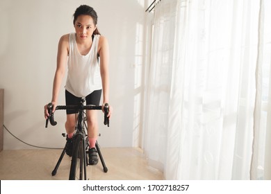 Asian Woman Cyclist. She Is Exercising In Home. She Cycling On The Trainer 