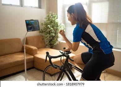 Asian Woman Cyclist. She Is Exercising In The Home.By Cycling On The Trainer And Play Online Bike Games.She Is Glad