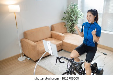 Asian Woman Cyclist. She Is Exercising In The Home.By Cycling On The Trainer And Play Online Bike Games.She Is Glad