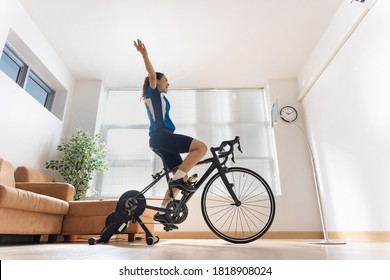 Asian Woman Cyclist. She Is Exercising In The Home.By Cycling On The Trainer And Play Online Bike Games.She Is
Glad