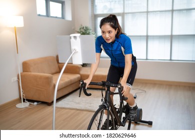 Asian Woman Cyclist. She Is Exercising In The Home.By Cycling On The Trainer And Play Online Bike Games.