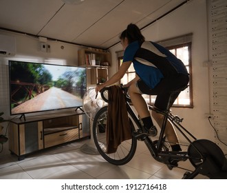 Asian Woman Cyclist. She Is Exercising At Home. She Is Playing Games In The Virtual World.