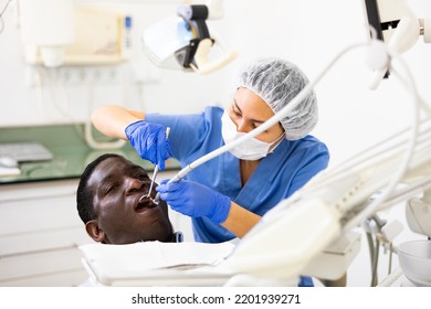 Asian Woman Dentist Examining Oral Cavity Of African-american Man Patient With Special Tools In Dental Clinic.