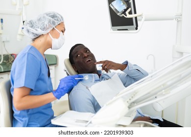 Asian Woman Dentist Listening To Patient During Consultation. African-american Man Pointing At Tooth With Problem.