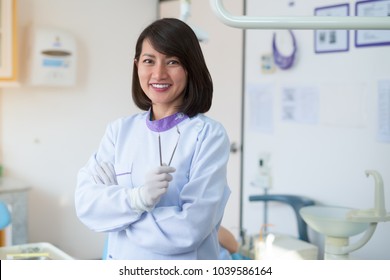 Asian Woman Dentist Stood Smiling And Holding A Dental Tool In A Hospital.