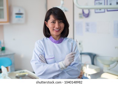 Asian Woman Dentist Stood Smiling And Holding A Dental Tool In A Hospital.