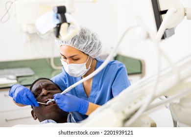 Asian Woman Dentist Using Tools For Tooth Repairing On African-american Man Patient In Clinic.