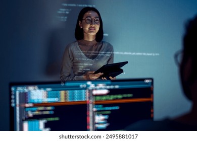 asian woman developers collaborating on a coding project, with one member presentation at code projected on the wall while the other works on multiple computer screens - Powered by Shutterstock