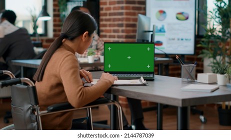 Asian Woman With Disability Using Greenscreen On Laptop, Working With Isolated Chromakey And Mockup Template. Person In Wheelchair Looking At Blank Copyspace Background On Display.