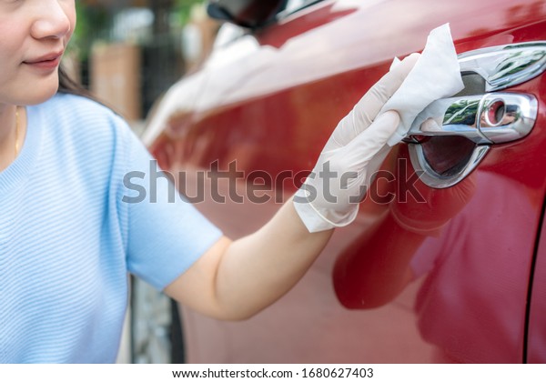 Asian woman disinfecting door handle of red car by\
disinfectant disposable wipes from box. Prevent the virus and\
bacterias, Prevent covid19, corona virus, Alcohol Sanitizer.\
Hygiene concept at home.