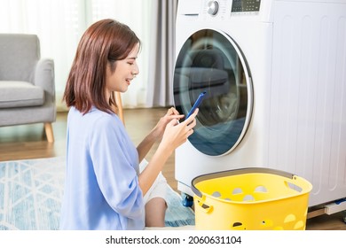 Asian Woman Do The Laundry In Smart Washing Machine And Use Smartphone Operate It At Home