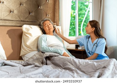 Asian woman doctor examine patient use infrared thermometer measured temperature in senior woman ear in bedroom. Nurse visit and checking elderly patient health at home. Home medical therapy concept. - Powered by Shutterstock