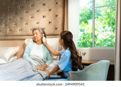 Asian woman doctor examine patient use infrared thermometer measured temperature in senior woman ear. Nurse visit and checking elderly patient health at home. Home medical caregiving service concept. - Powered by Shutterstock