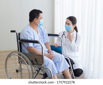 Asian Woman Doctor Explain And Suggest Some Information With A Man Patient Who Sit On A Wheel Chair. They Wear A Medical Face Mask While Talking Together In Hospital.