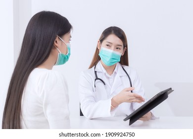 Asian Woman Doctor Give Counsel To Her Woman Patient Which Doctor Shows Information On Tablet While Both Wear Medical Face Mask In Hospital.