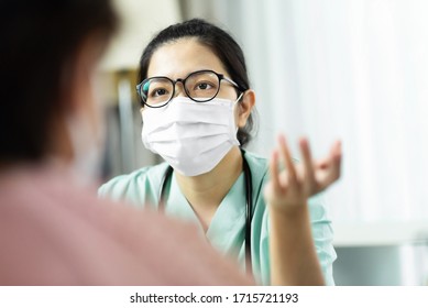 Asian Woman Doctor In Green Uniform Wear Eyeglasses And Surgical Mask Talking, Consulting And Giving Advice To Elderly Female Patient At The Hospital. Symptoms, Disease, Flu, Covid-19, Coronavirus.