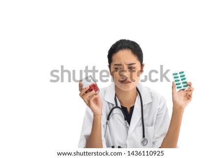A Asian woman doctor holding bottles and a pack of medicine in her hands looking unhappy, upset, and tired. In front of white isolated background.