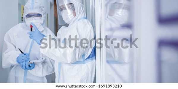 Asian woman doctor in personal protective suit\
or PPE with mask writing on quarantine patient chart, holding test\
tube with blood sample for screening coronavirus. Coronavirus,\
covid-19 concept.