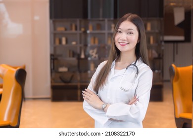 Asian Woman Doctor Standing Smile In A Good Mood With Arms Crossed In The Office Room In The Hospital. Wearing A White Robe And Stethoscope.