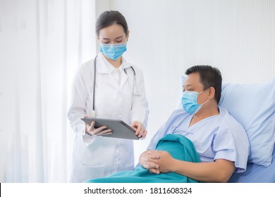 Asian Woman Doctor Talking With A Man Patient Who He Is On Bed About His Pain And Symptom In Hospital.  They Wear A Medical Face Mask To Protect Respiration System (Covid-19).
