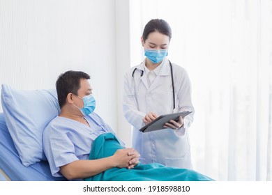 Asian Woman Doctor Talking With A Man Patient Who He Is On Bed About His Pain And Symptom In Hospital. They Wear A Medical Face Mask To Protect Respiration System (Covid-19).