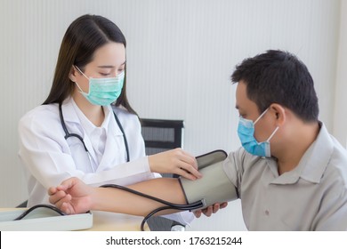 Asian Woman Doctor Uses A Blood Pressure Meter With A Man Patient  To Check His Health At Hospital. They Wear A Medical Face Mask To Protect Respiration System Infection.