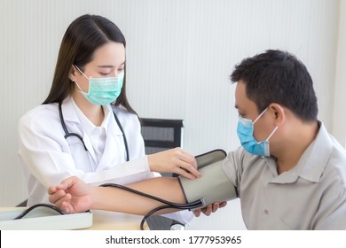 Asian Woman Doctor Uses A Blood Pressure Meter With A Man Patient  To Check His Health At Hospital. They Wear A Medical Face Mask To Protect Respiration System Infection.