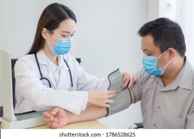 Asian Woman Doctor Uses A Blood Pressure Meter With A Man Patient  To Check His Health At Hospital. They Wear A Medical Face Mask To Protect Respiration System Infection. 