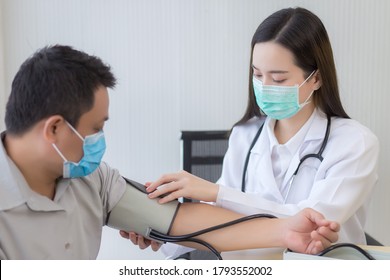 Asian Woman Doctor Uses A Blood Pressure Meter With A Man Patient  To Check His Health At Hospital. They Wear A Medical Face Mask To Protect Respiration System Infection.