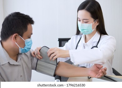 Asian Woman Doctor Uses A Blood Pressure Meter With A Man Patient  To Check His Health At Hospital. They Wear A Medical Face Mask To Protect Respiration System Infection.