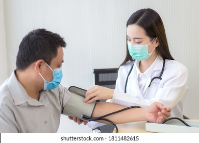 Asian Woman Doctor Uses A Blood Pressure Meter With A Man Patient  To Check His Health At Hospital. They Wear A Medical Face Mask To Protect Respiration System Infection.