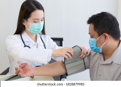 Asian Woman Doctor Uses A Blood Pressure Meter With A Man Patient  To Check His Health At Hospital. They Wear A Medical Face Mask To Protect Respiration System Infection.