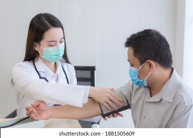 Asian Woman Doctor Uses A Blood Pressure Meter With A Man Patient  To Check His Health At Hospital. They Wear A Medical Face Mask To Protect Respiration System Infection.