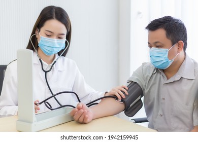 Asian Woman Doctor Uses A Blood Pressure Meter With A Man Patient To Check His Health At Hospital. They Wear A Medical Face Mask To Protect Respiration System Infection.