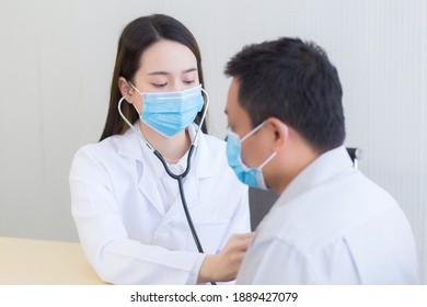 Asian woman doctor uses stethoscope to check up health of the man patient while both wear medical face mask to prevent respiratory system infectious from pathogens or Covid-19.  - Shutterstock ID 1889427079