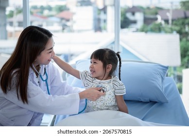 Asian Woman Doctor Is Using A Stethoscope Listen To Heart Rate Of A 3 Year Old Patient Which Sitting On The Patient's Bed, With Blur Background, To Health Care And Children Concept.