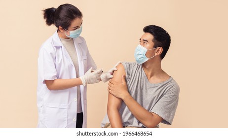 Asian Woman Doctor Wearing Face Mask And Gloves Giving Vaccine To A Man On Brown Background With Space. Asian Man Getting Vaccinated By A Medical Professional.