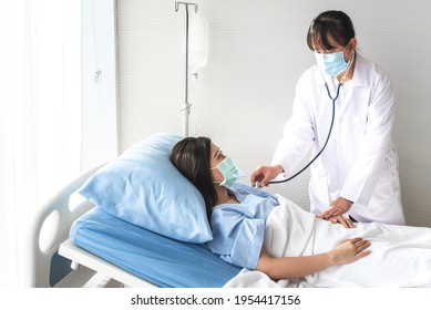 Asian Woman Doctor Wearing A Surgical Mask, Is Using A Stethoscope Listen To Heart Rate Of A Woman Patient Who Came To Treat The Flu, Which Is Pandemic, To Health Care And Insurance Concept.