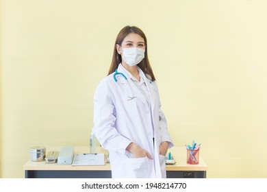 Asian Woman Doctor Who She Has A Black Long Hair, Wears A Medical Face Mask And Wear A Stethoscope And A White Lab Coat As A Uniform While Hand Pickpocket At Office Room At Hospital.