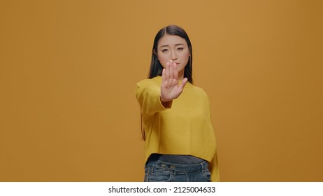 Asian woman doing rejection gesture with hand in front of camera, concept of refusing and not accepting. Person showing stop sign with palm, being in denial and expressing restriction.