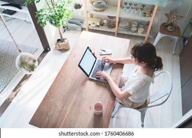 Asian woman doing remote work with laptop at dining table at home - Powered by Shutterstock