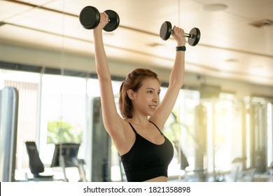 Asian woman doing shoulder press exercise, lifting dumbbell over head. - Powered by Shutterstock