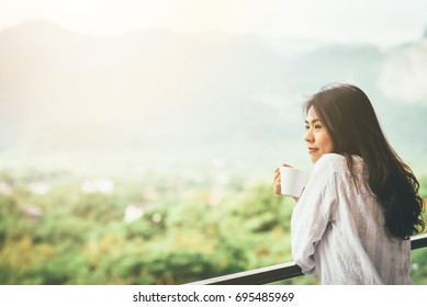 Asian Woman Drinking A Cup Of Coffee And Enjoy Nature View In Morning With Sunlight