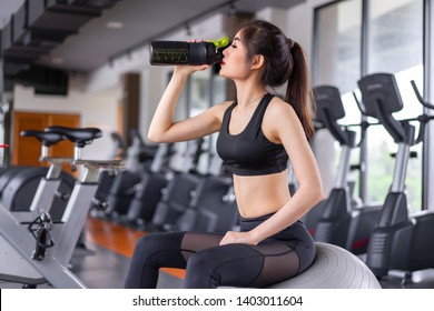 Asian Woman Drinking Protein Shake From Bottle After Workout Exercise For Muscle At Fitness Gym Healthy Lifestyle Bodybuilding Sitting On Fitness Ball