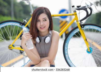 Asian Woman Drinking Water After Riding An Exercise Bike On The Road.