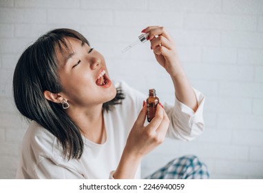Asian woman dripping cbd oil into her mouth. Close up asian women taking CBD Oil for sleep. Medical cannabis. Vitamins and supplements