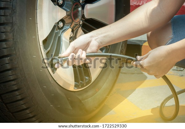 Asian woman driver\
checking air pressure filling air into a car tire to increase\
pressure car tire close up. The right tire pressure reduces\
accidents, increases\
safety.