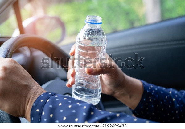 Asian woman driver\
holding bottle for drink water while driving a car. Plastic hot\
water bottle cause fire.