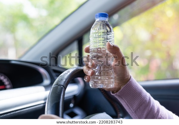 Asian woman driver\
holding bottle for drink water while driving a car. Plastic hot\
water bottle cause fire.